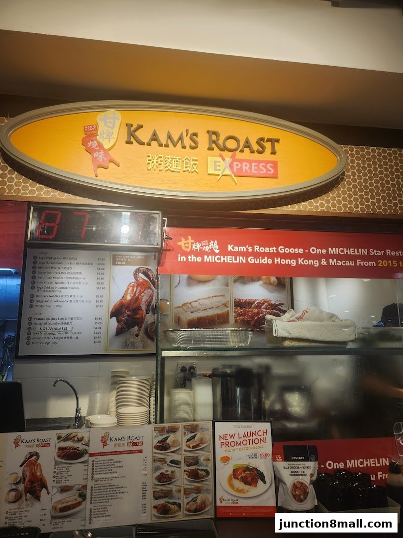 A food stall with a prominent sign for Kam's Roast Express, showcasing roasted meats and menu items.