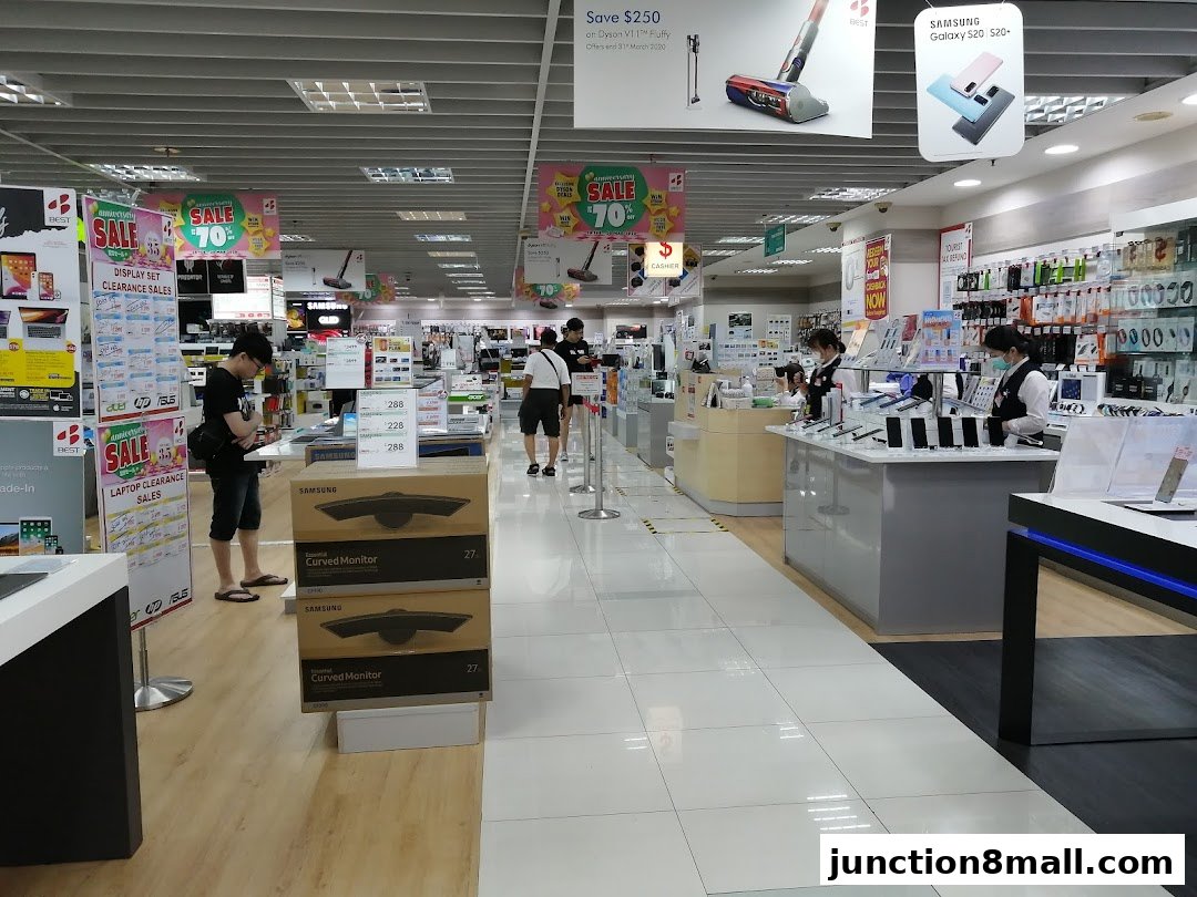 Interior view of an electronics store with various products and displays, including monitors and phones.