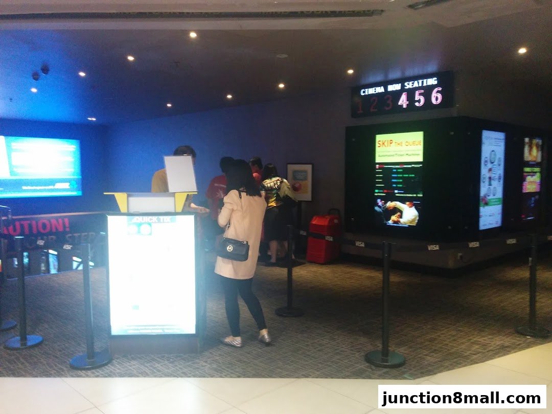 People queuing at a cinema ticket counter with digital displays showing movie information.