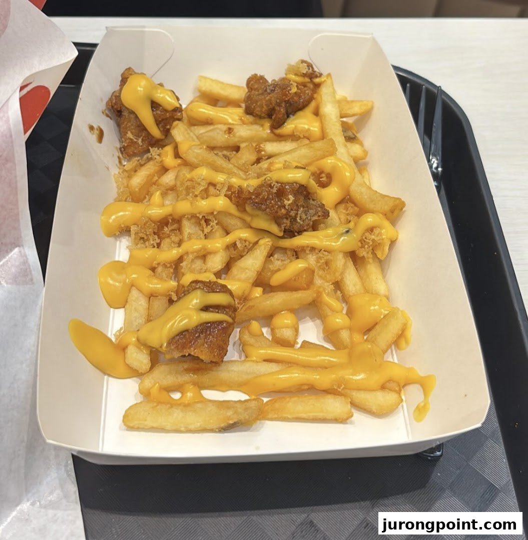 A close-up of crispy fries topped with melted cheese sauce and savory chicken pieces in a white tray.