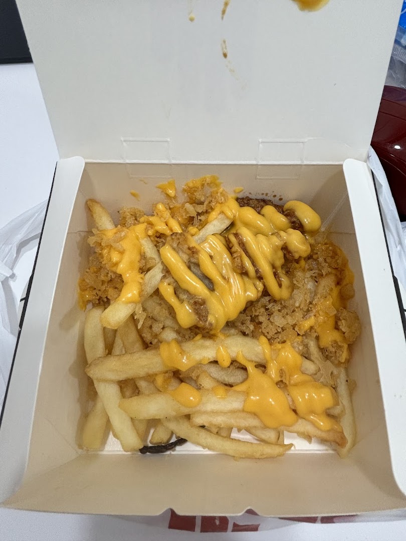 A close-up of crispy chicken and fries generously topped with rich cheese sauce in a takeaway box.