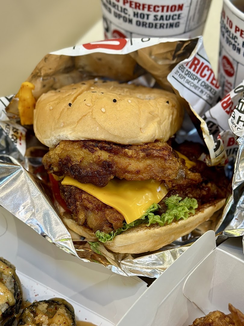 A close-up of a delicious crispy chicken burger with cheese and lettuce, served in foil packaging.