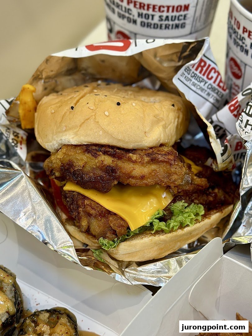 A close-up of a delicious crispy chicken burger with cheese and lettuce, served in foil packaging.