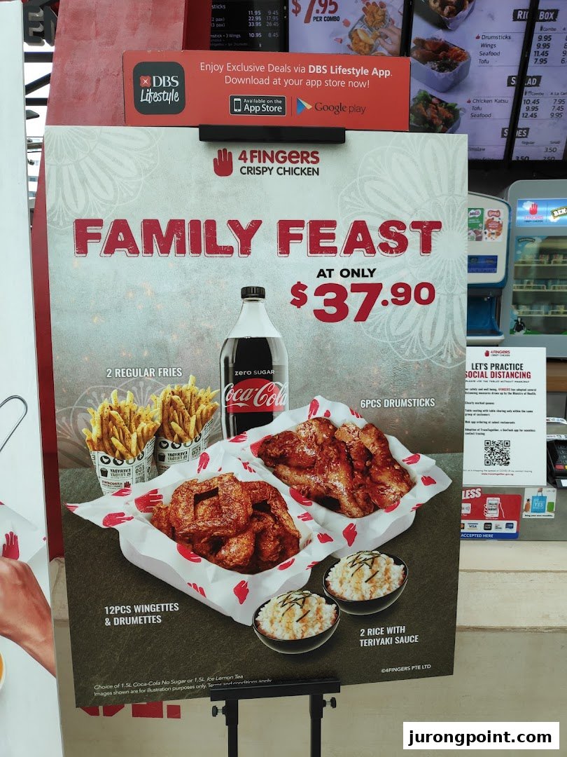 A promotional standee for 4Fingers Crispy Chicken's 'Family Feast' combo, featuring chicken, fries, rice, and a drink.
