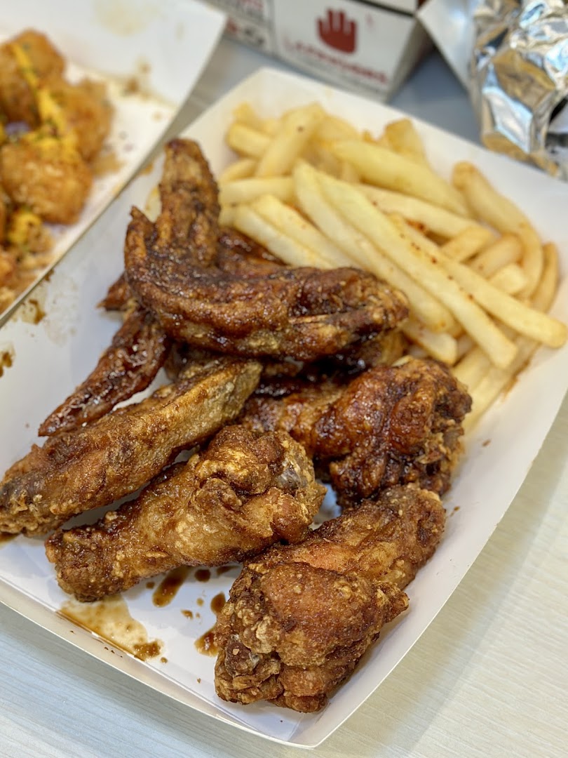 A close-up of crispy chicken wings and golden fries in a takeout box from 4Fingers.