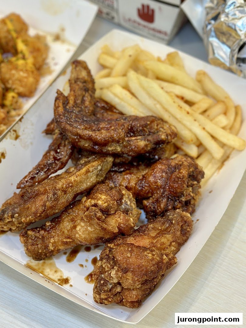 A close-up of crispy chicken wings and golden fries in a takeout box from 4Fingers.