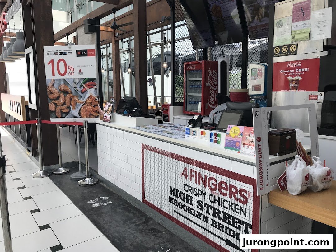 The 4Fingers Crispy Chicken counter with branding, a Coca-Cola fridge, and a promotional offer poster.