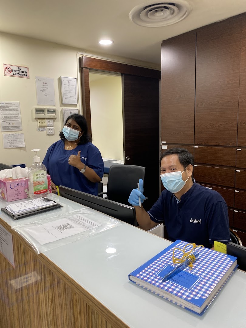 Two friendly AcuMed Medical staff members, wearing masks, give thumbs up from behind the reception desk.
