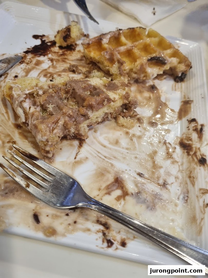 A partially eaten waffle with chocolate sauce and cream on a white plate, with a fork.