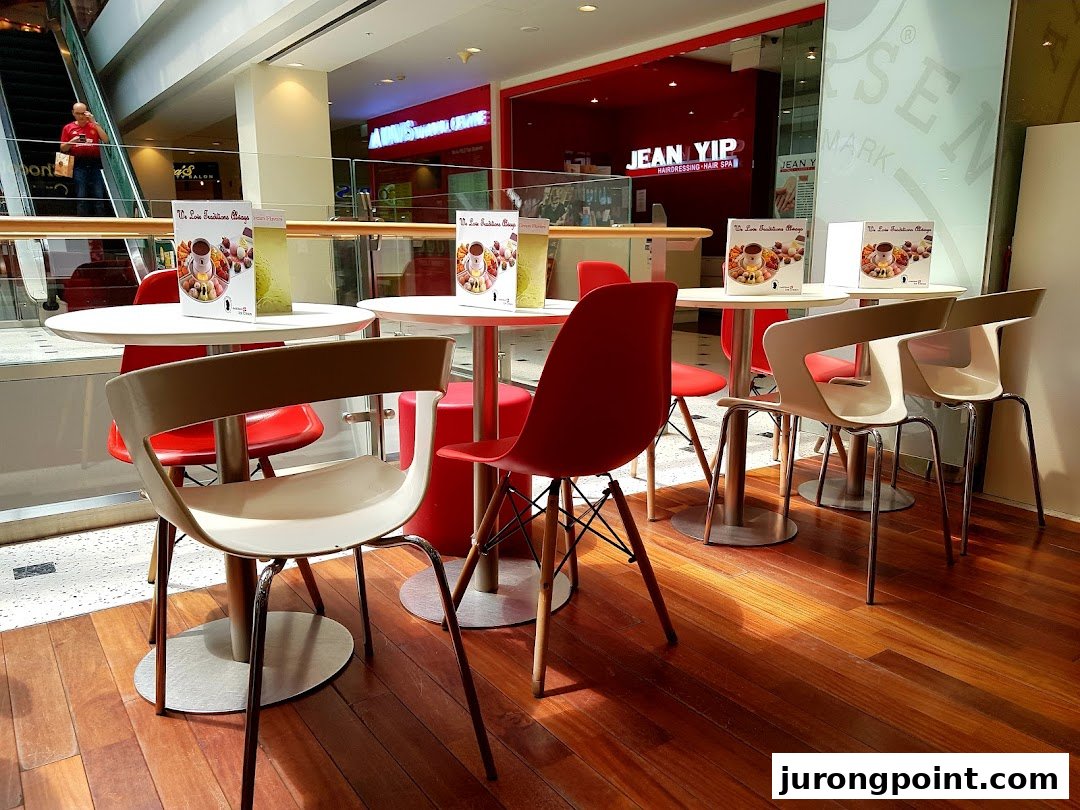 A cozy seating area with white tables and red and cream chairs, offering a view of the mall.