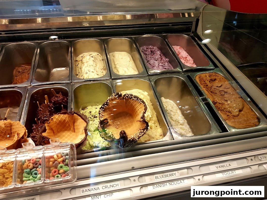 A vibrant display of various ice cream and gelato flavors with toppings in a dessert shop.