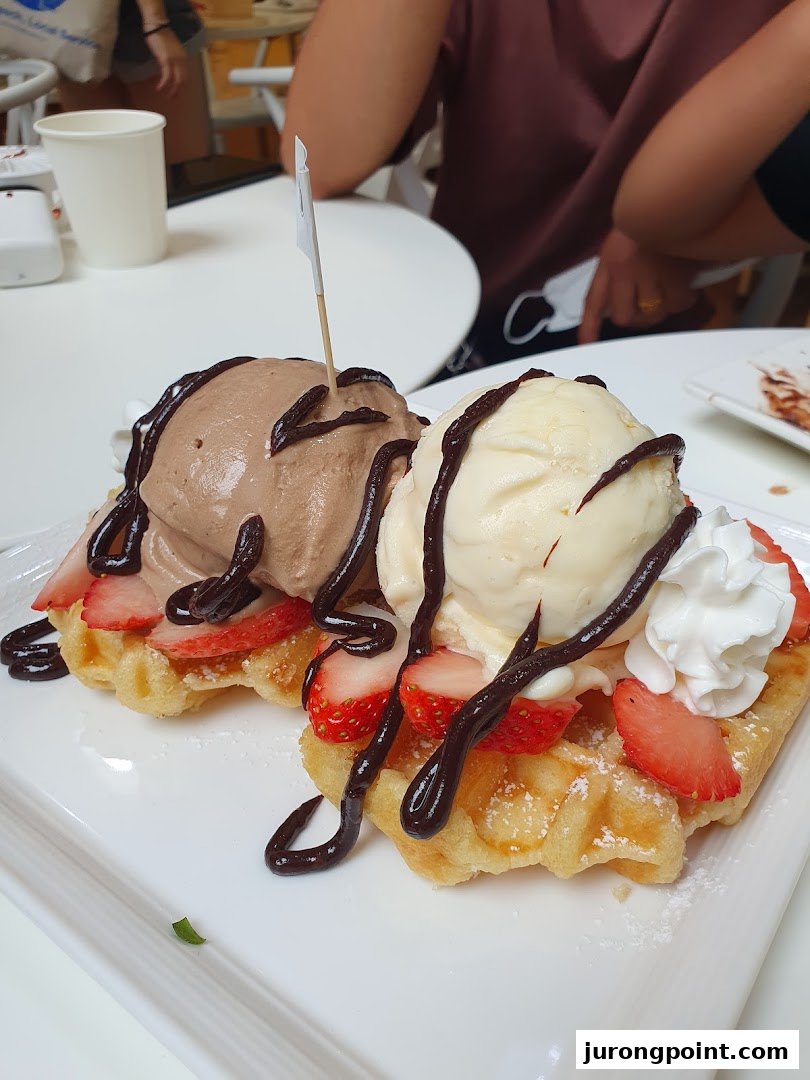 Two delicious waffles topped with strawberries, chocolate and vanilla ice cream, and chocolate sauce.