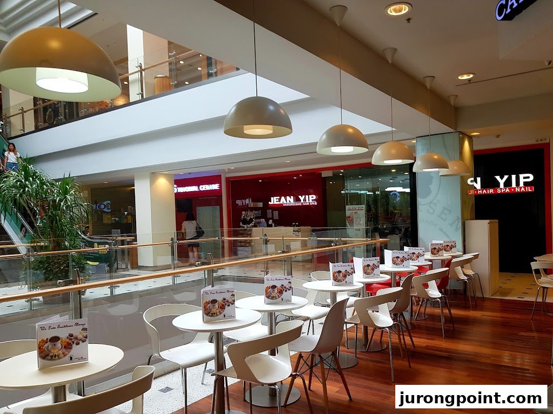 A cozy cafe seating area with white tables and chairs inside a bustling shopping mall.