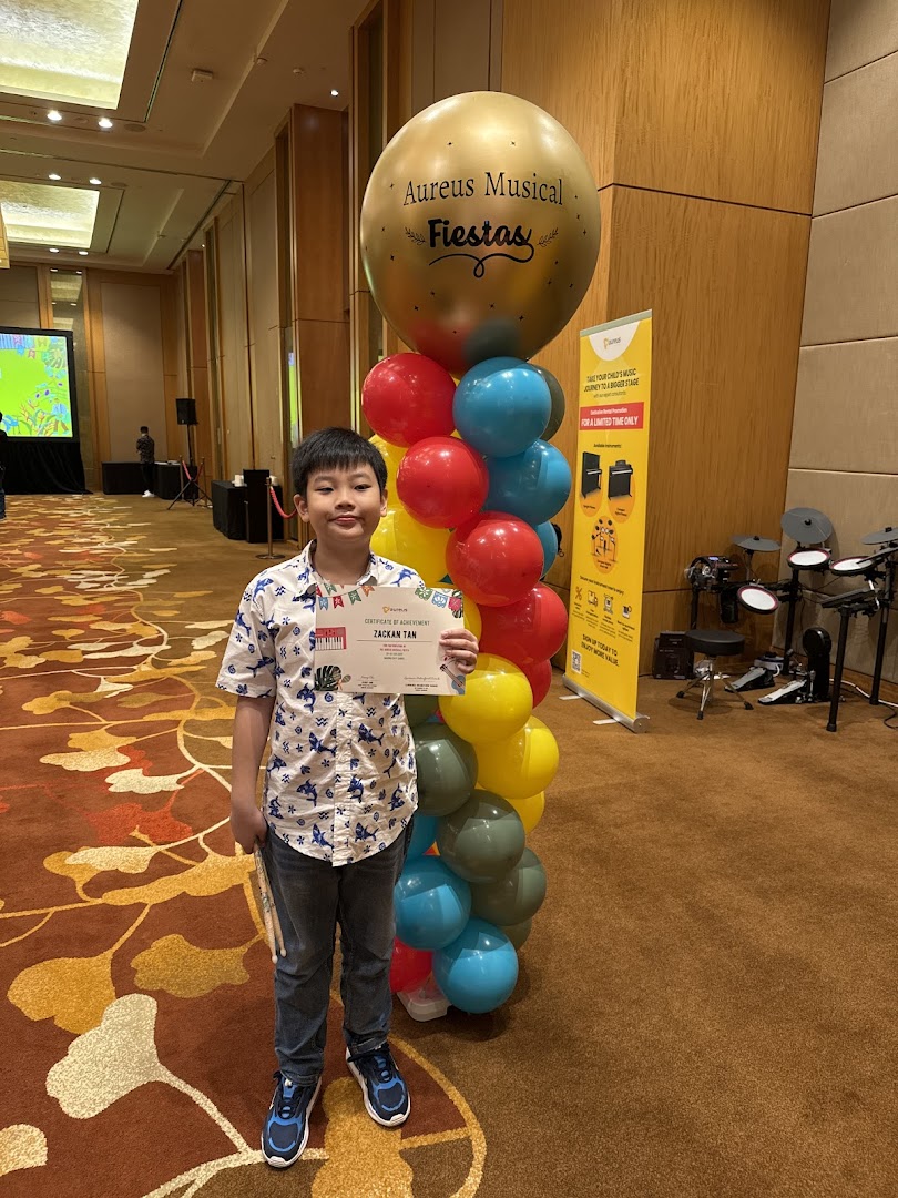 A child proudly holds a certificate at an Aureus Musical Fiestas event.