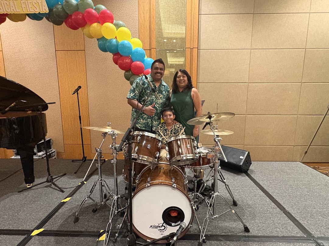 A family poses with a drum set and piano on a stage with a colorful balloon arch.