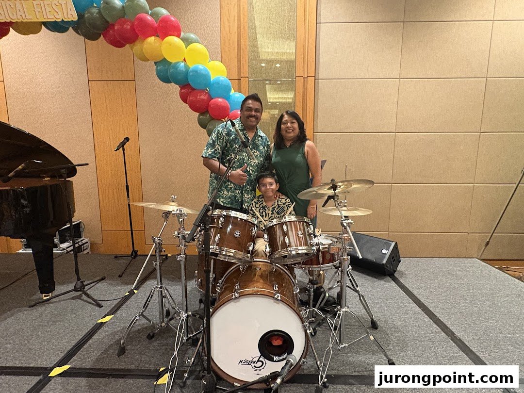 A family poses with a drum set and piano on a stage with a colorful balloon arch.