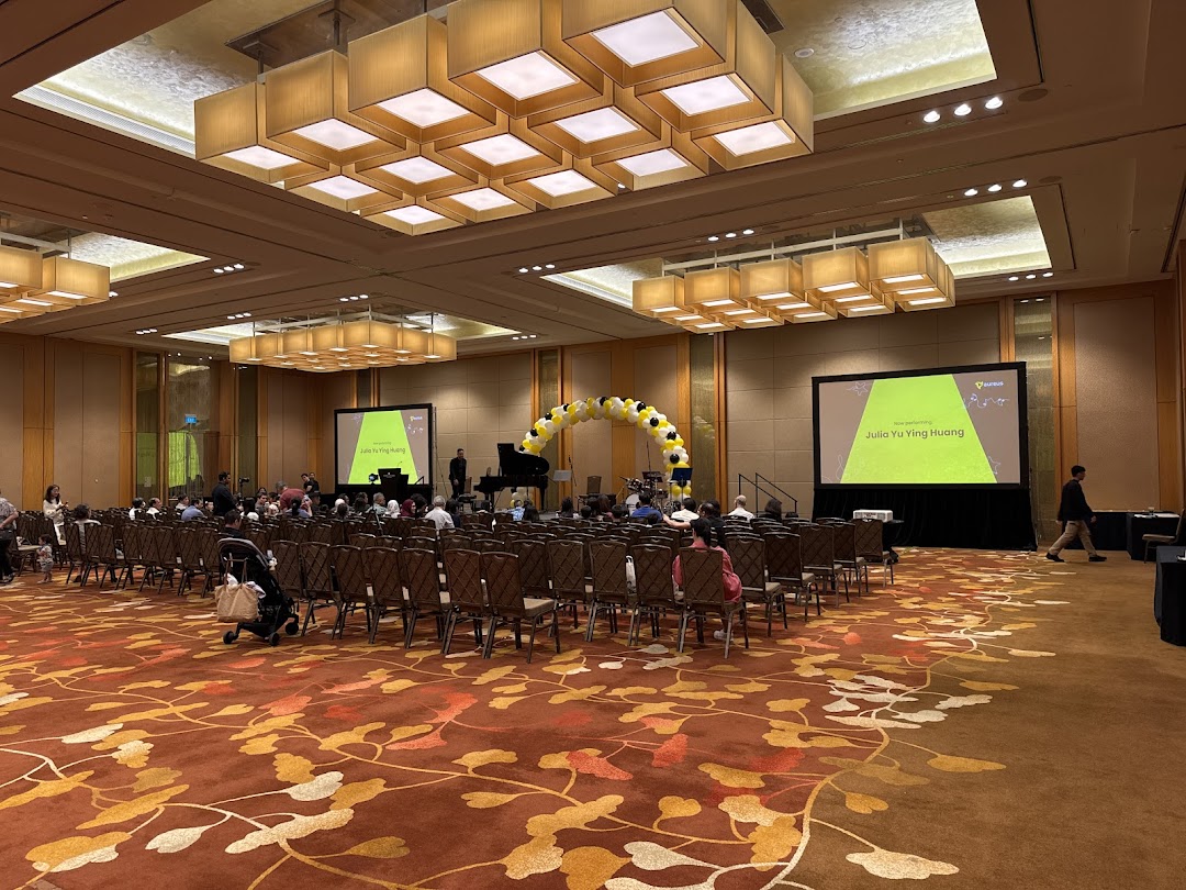 A large hall set up for an Aureus Academy event with a stage, screens, and audience seating.