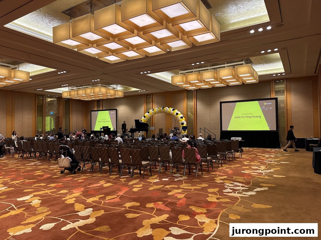 A large hall set up for an Aureus Academy event with a stage, screens, and audience seating.