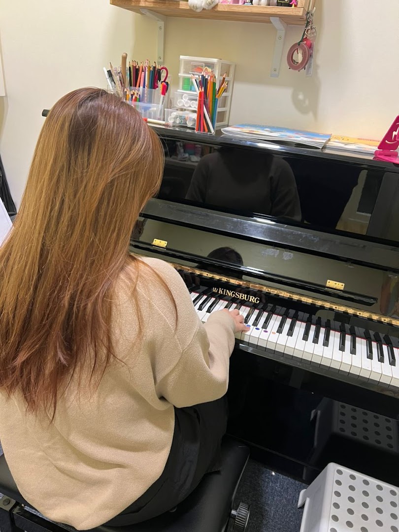 A student practices piano on a Kingsburg piano at Aureus Academy, with art supplies nearby.
