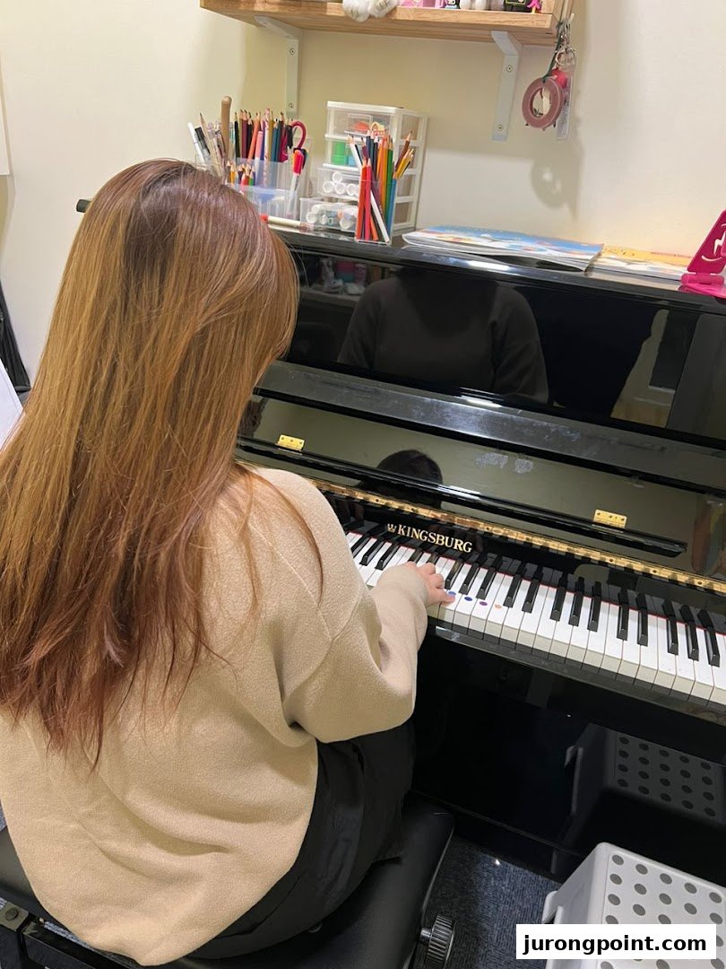 A student practices piano on a Kingsburg piano at Aureus Academy, with art supplies nearby.