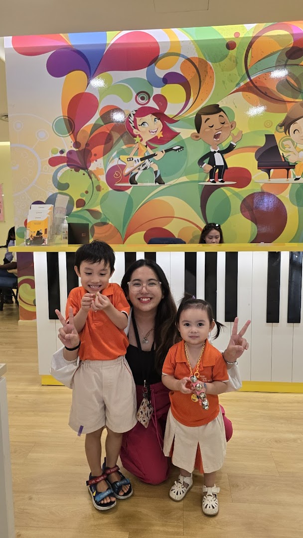 A woman and two children pose happily in front of a vibrant, music-themed counter at Aureus Academy.