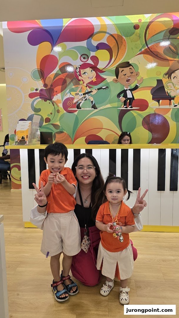 A woman and two children pose happily in front of a vibrant, music-themed counter at Aureus Academy.