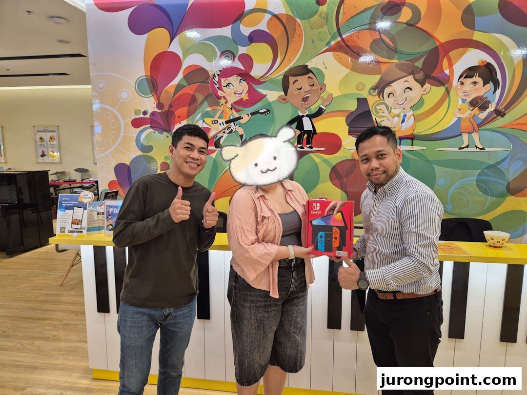 Three people, one receiving a Nintendo Switch, in a vibrant music academy setting with a piano-themed counter.