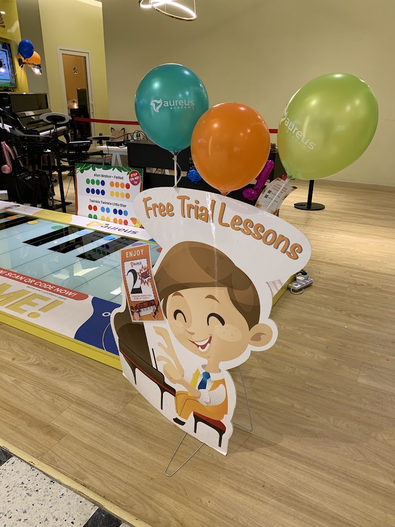 Interior view of Aureus Academy featuring promotional balloons, a floor piano, and a 'Free Trial Lessons' standee.