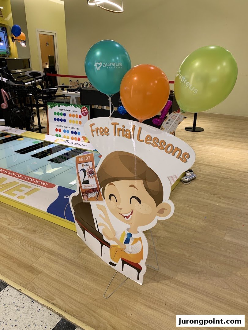 Interior view of Aureus Academy featuring promotional balloons, a floor piano, and a 'Free Trial Lessons' standee.