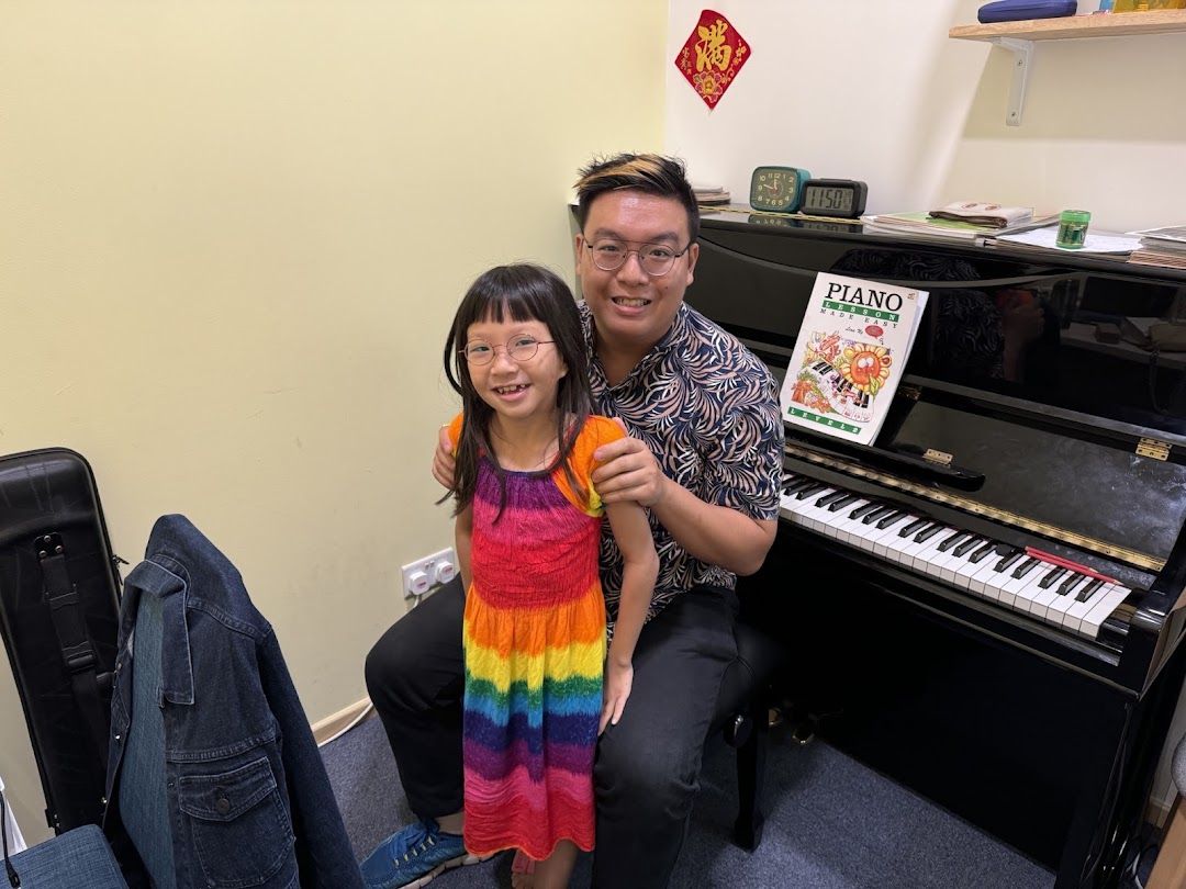 An instructor and a young student smiling next to a piano during a music lesson.