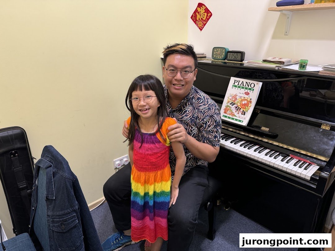 An instructor and a young student smiling next to a piano during a music lesson.