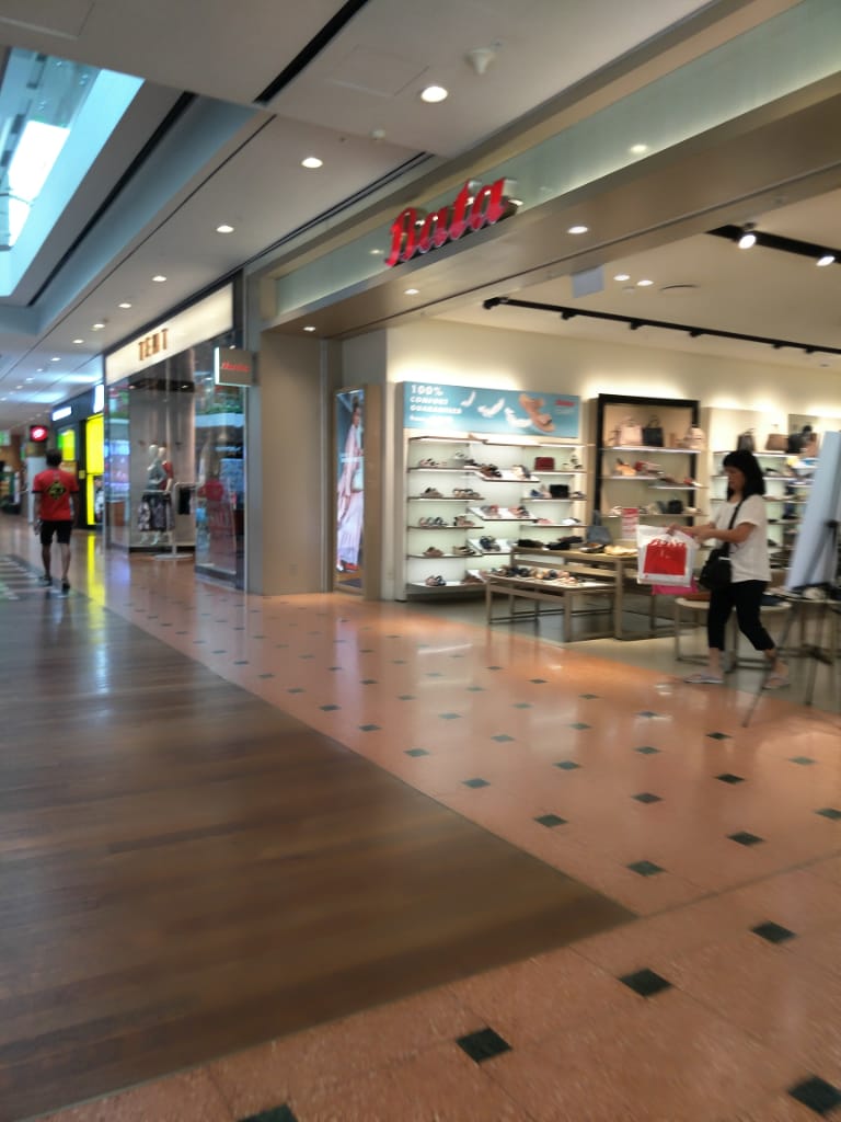 View of the Bata shoe store interior from the mall corridor with a shopper inside.