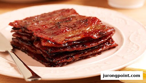 A stack of glossy, caramelized bak kwa (barbecued meat slices) on a light pink plate with a serving spatula.