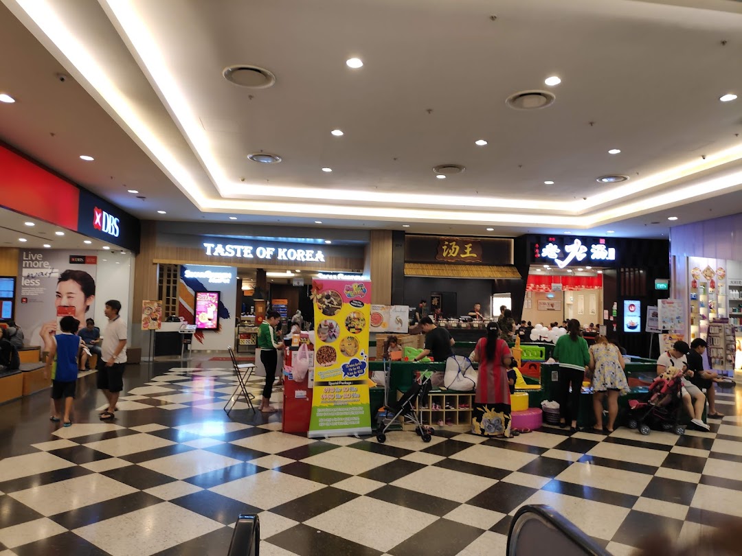 A bustling mall interior featuring various shop fronts, a promotional stand, and shoppers.
