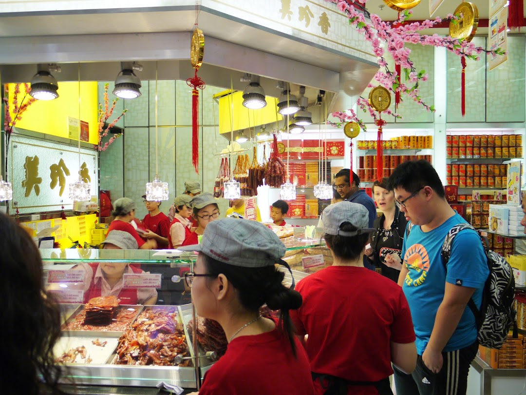 Customers and staff interact in a bustling Bee Cheng Hiang shop, showcasing fresh bak kwa and traditional Chinese decor.