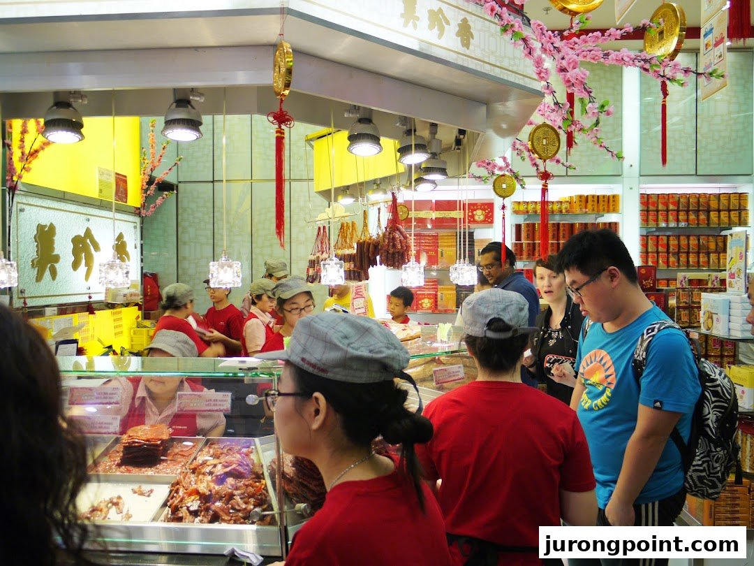 Customers and staff interact in a bustling Bee Cheng Hiang shop, showcasing fresh bak kwa and traditional Chinese decor.