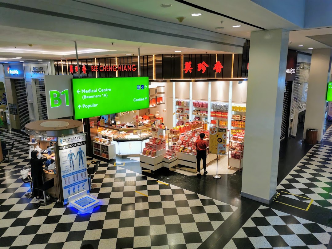 A bustling Bee Cheng Hiang shop in a mall, showcasing its products, with a 'Custom Feet' booth nearby.