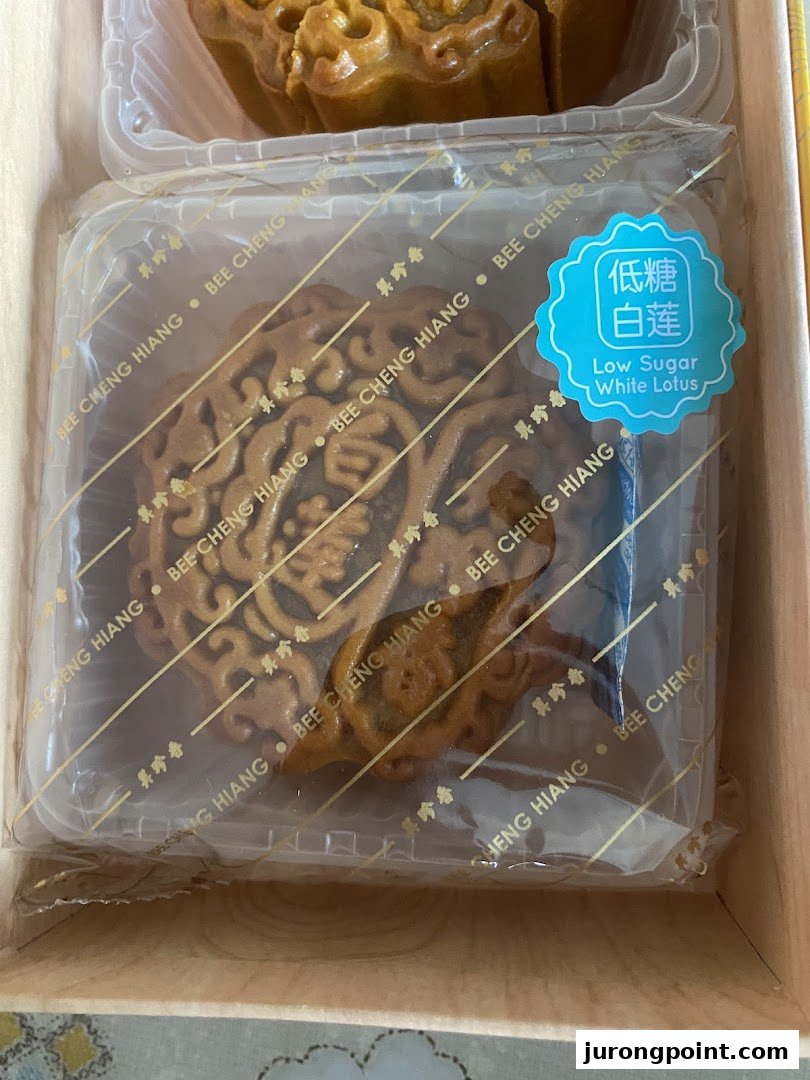 A Bee Cheng Hiang low sugar white lotus mooncake in its individual packaging, part of a gift box.
