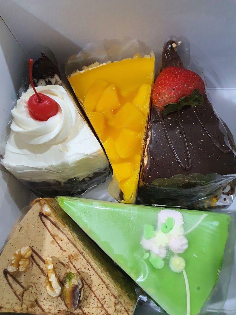 A box filled with five colorful and delicious-looking cake slices, including mango, chocolate, and cream.