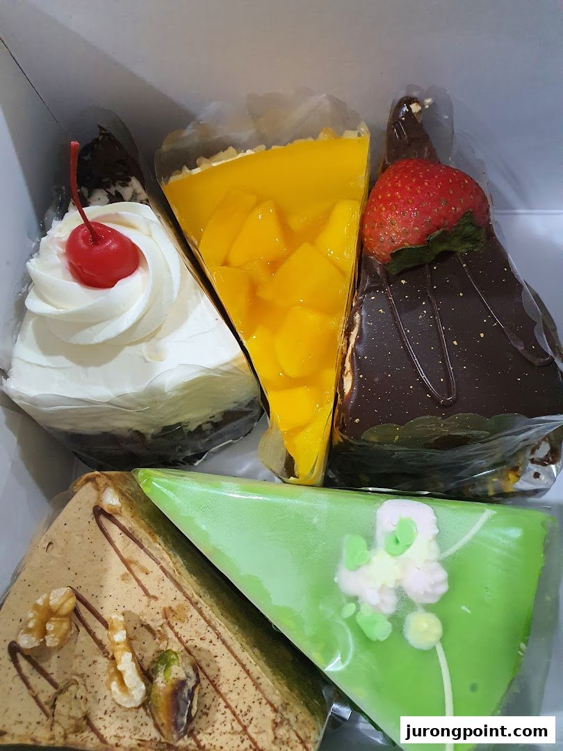A box filled with five colorful and delicious-looking cake slices, including mango, chocolate, and cream.