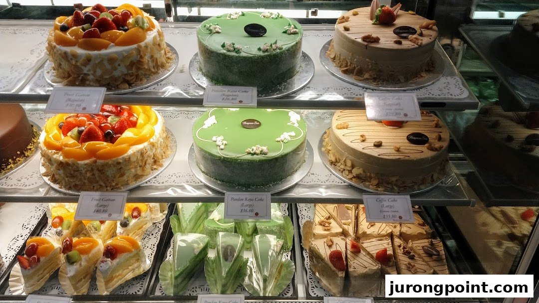 A vibrant display case showcasing a variety of beautifully decorated cakes, including fruit, pandan, and coffee flavors.