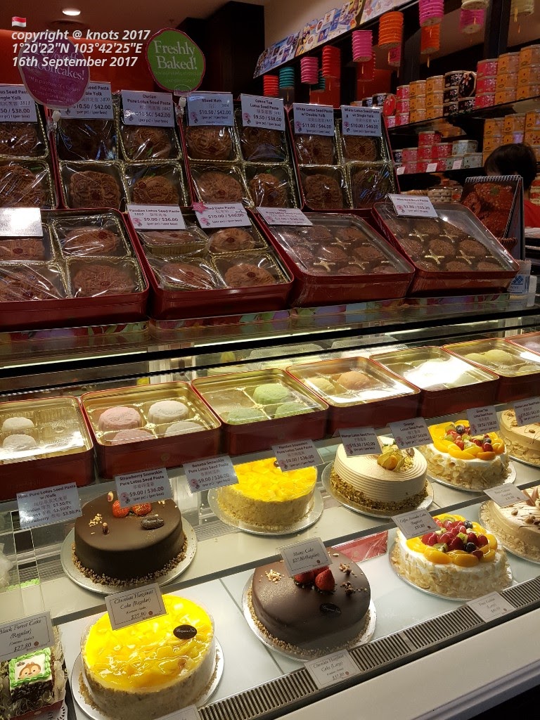 A vibrant display of freshly baked mooncakes, snowskin pastries, and delicious cakes in a retail shop.