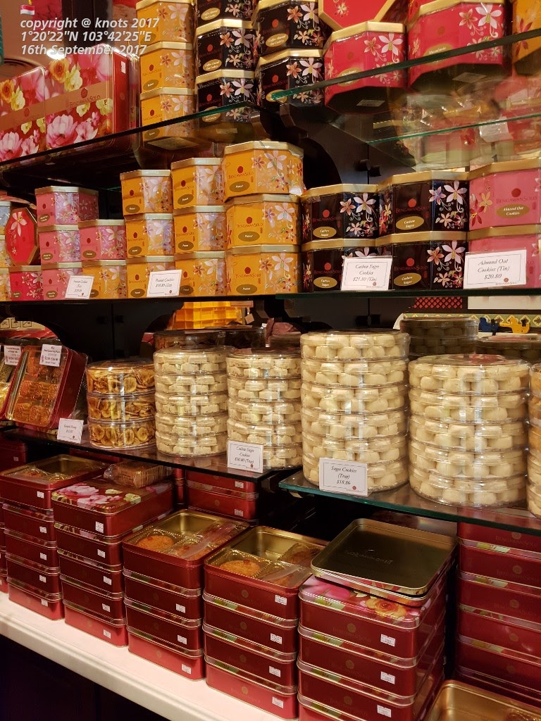 A vibrant display of traditional Indonesian cookies and pastries in decorative tins and clear containers.