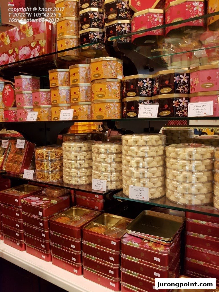 A vibrant display of traditional Indonesian cookies and pastries in decorative tins and clear containers.