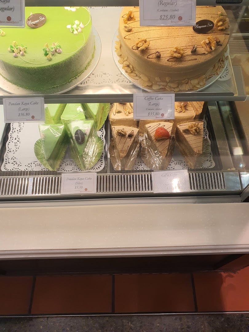 A display case showcasing a variety of delicious cakes, including Pandan Kaya and Coffee cakes, with visible price tags.