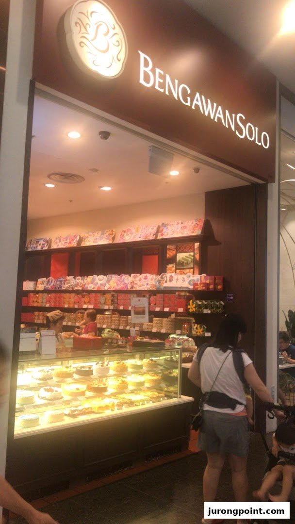A vibrant shop front of Bengawan Solo, showcasing a display of cakes and pastries, with customers entering.