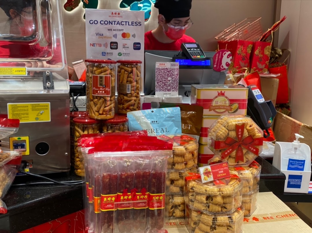 A shop counter at Bengawan Solo displaying a variety of packaged traditional snacks and treats, with a staff member.