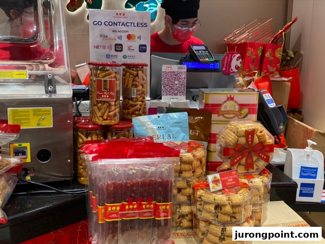 A shop counter at Bengawan Solo displaying a variety of packaged traditional snacks and treats, with a staff member.