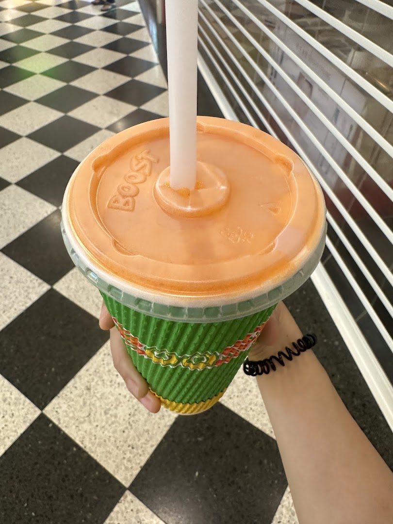 A hand holds a vibrant green Boost Juice cup with an orange lid and straw.