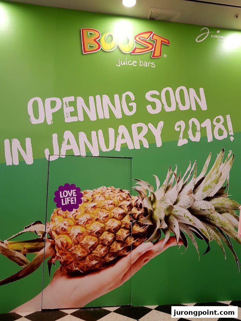 A vibrant green hoarding for Boost Juice announces its opening soon in January 2018, featuring a large pineapple.